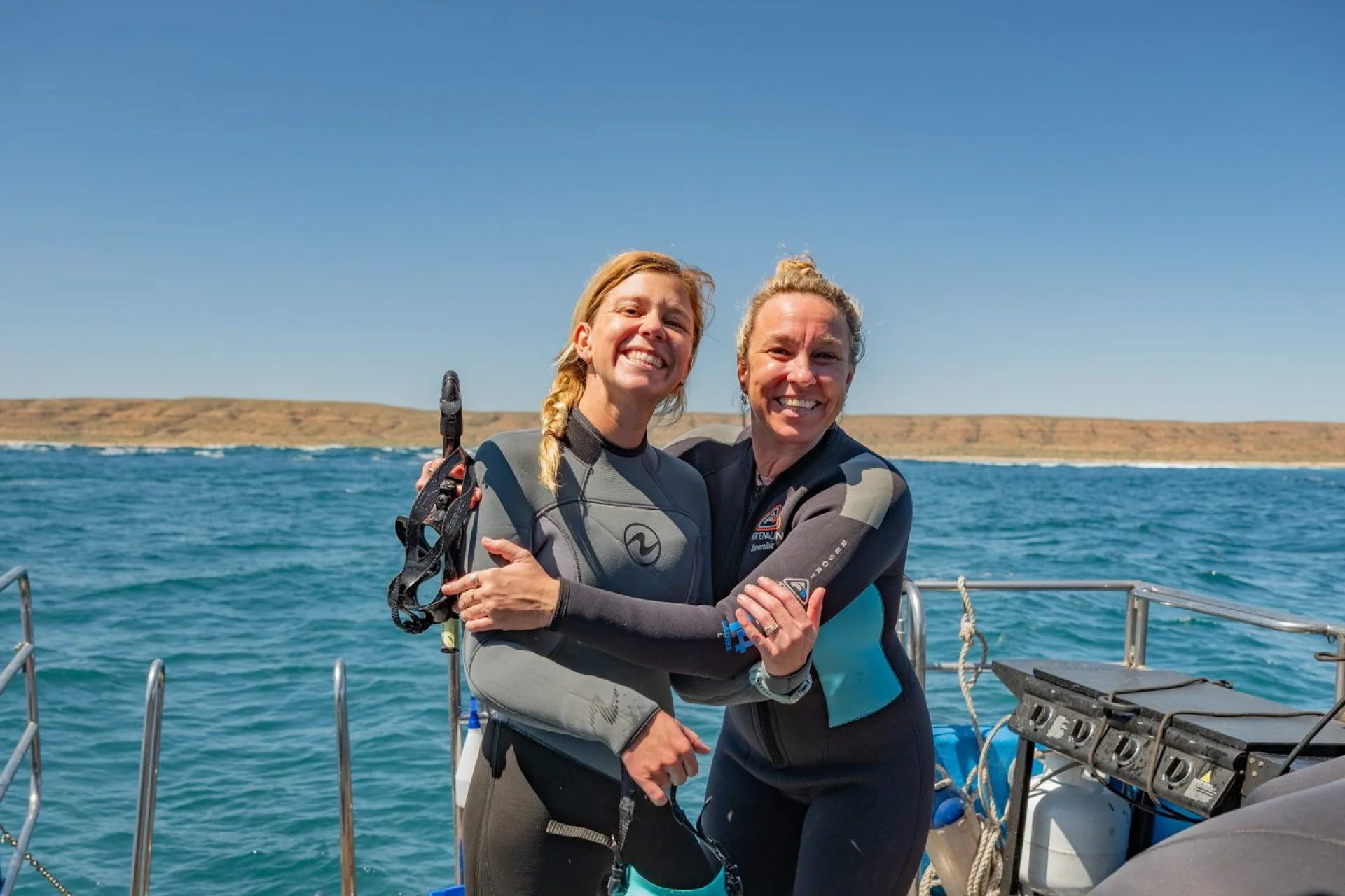 Two divers in wetsuits hugging on the deck