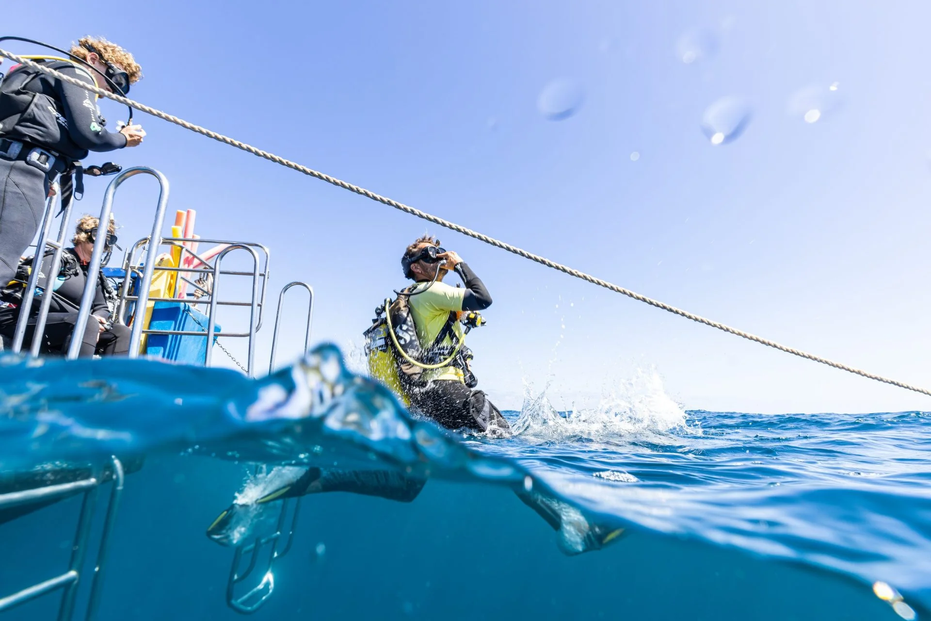 Over-under view of a diver landing in the water beside the boat